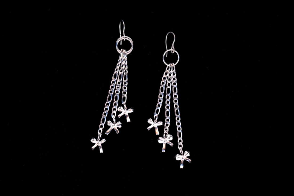 A pair of stainless steel chain-drop bow earrings with multiple small bows attached to figaro chains, displayed against a black background.