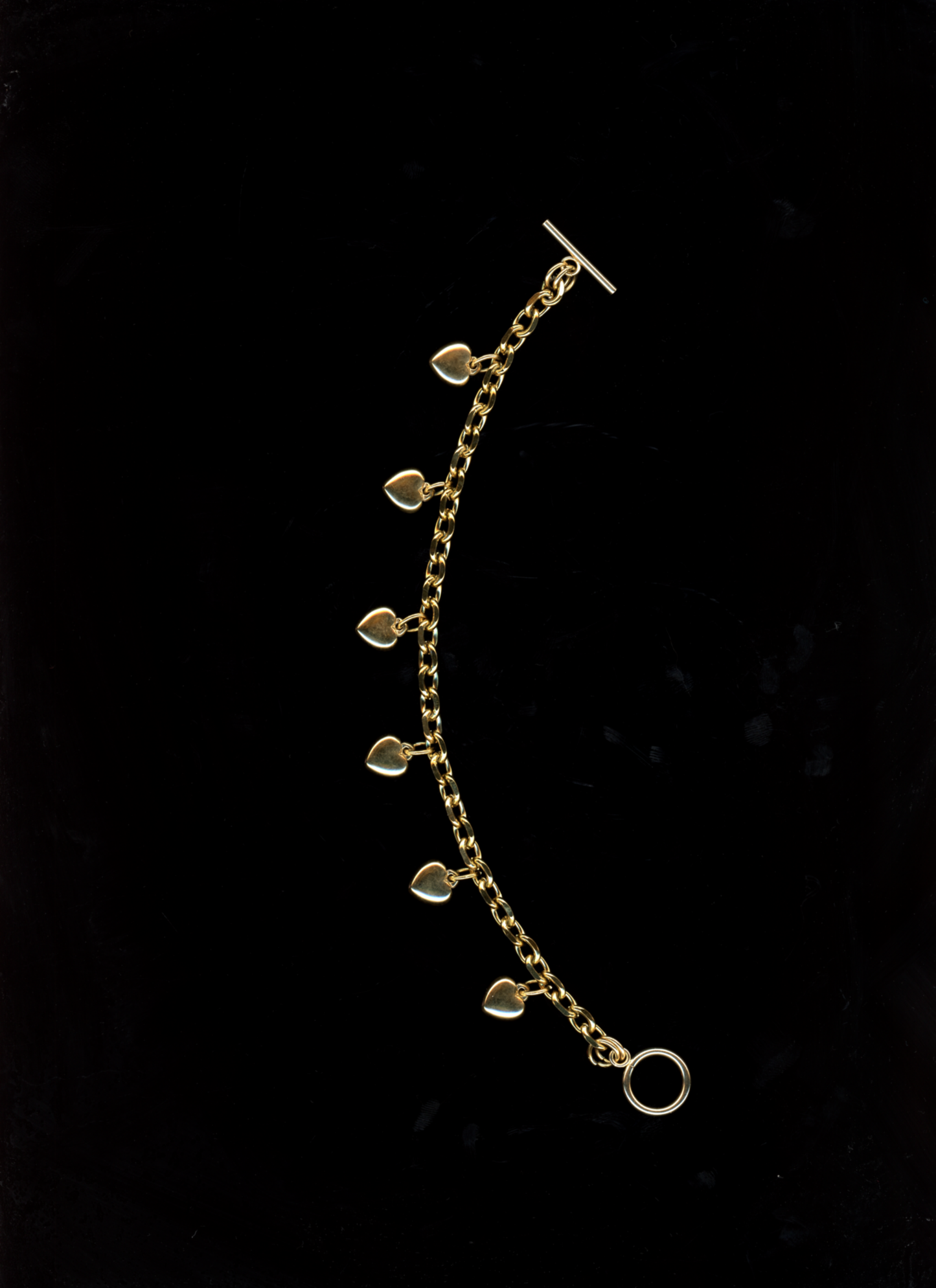 Gold bracelet with heart-shaped charms on a black background