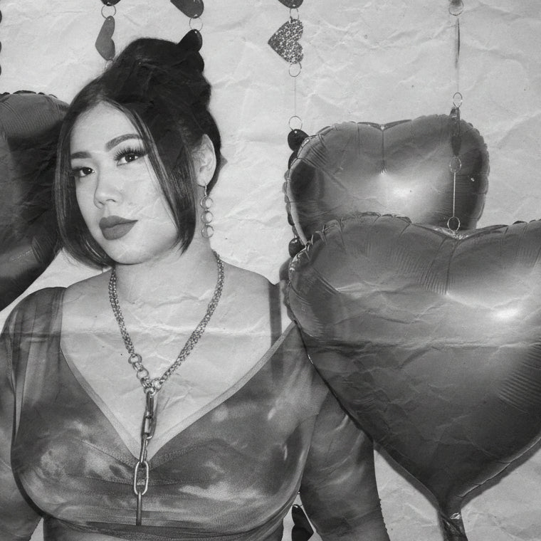 racheal wears the trinity drop earrings and aria necklace in a v neck top and high bun with bangs surrounded by heart shaped balloons and garlands in a black and white edit