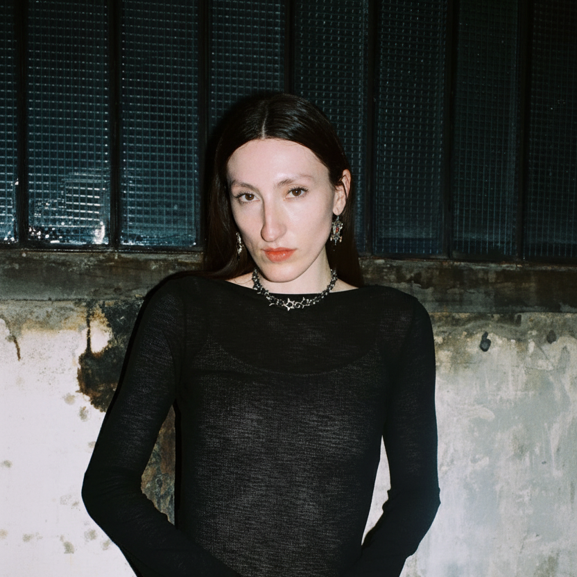 High fashion model wearing a black dress against a textured wall wearing a bywolfgang, chainmail star necklace