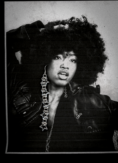 Person wearing a leather outfit with a detailed chain necklace and chainmail star earrings against a textured background