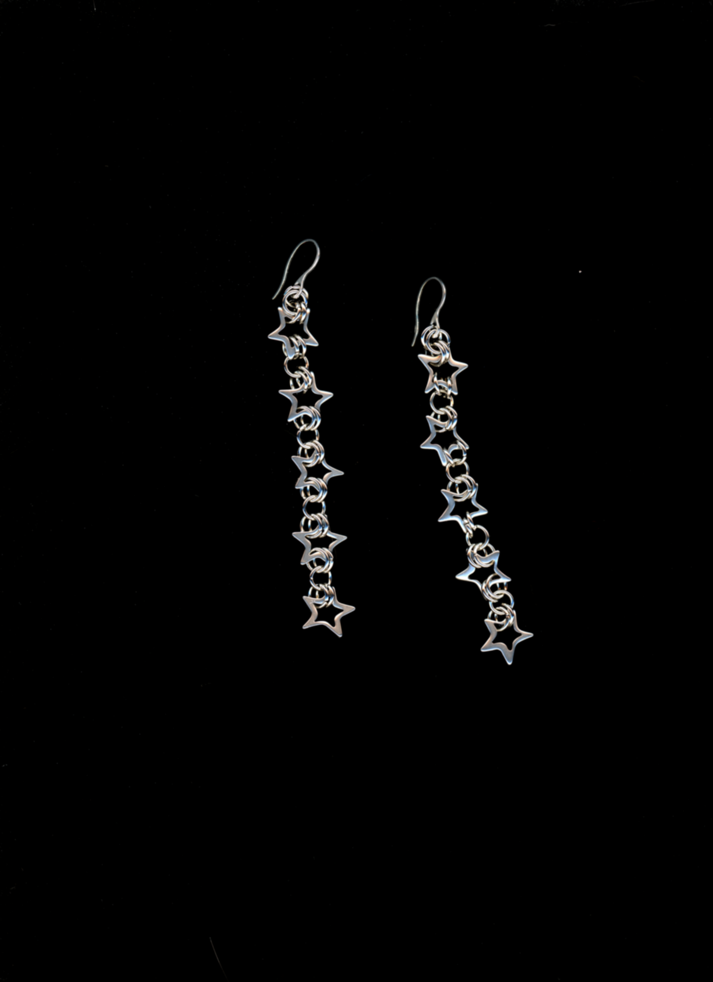 A pair of silver-colored star chainmail drop earrings with classic ear wire, displayed against a black background.