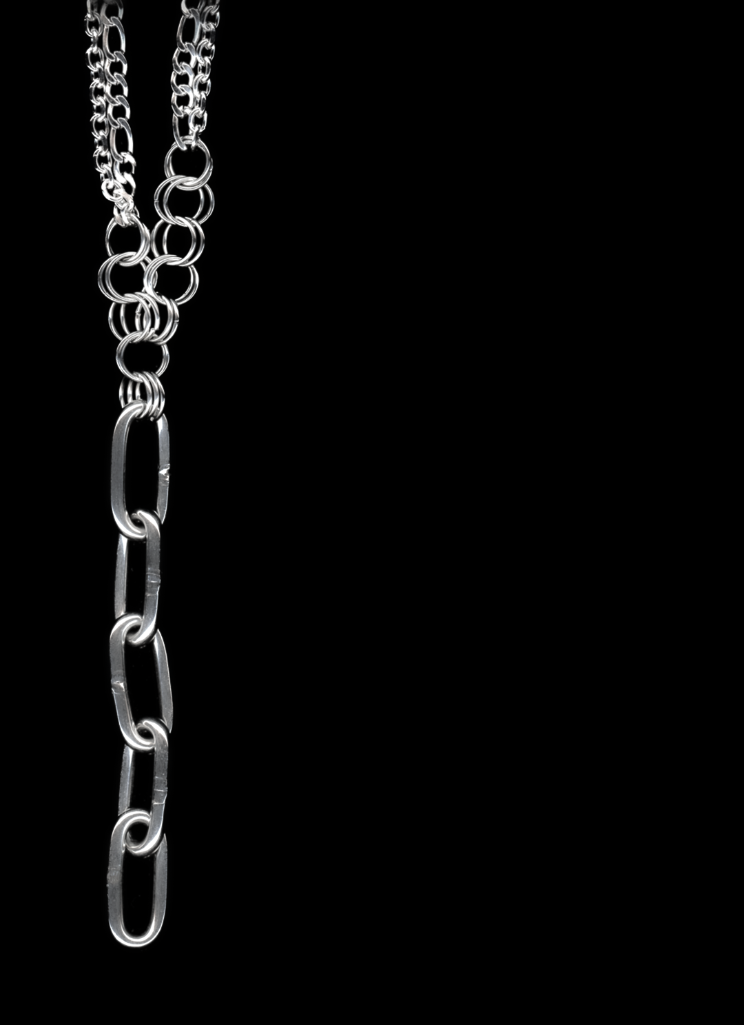 A silver Figaro chain lariat necklace with a diamond-cut chain pendant and chainmail detail, displayed against a black background.