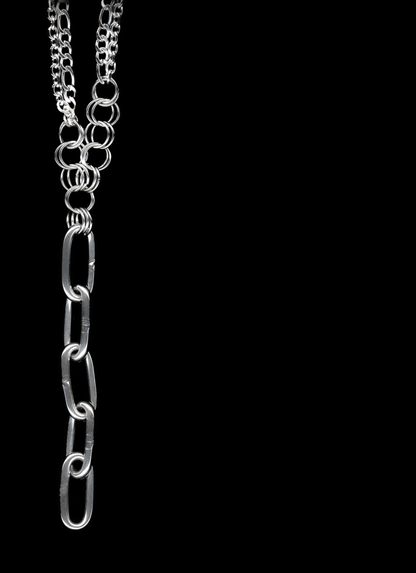 A silver Figaro chain lariat necklace with a diamond-cut chain pendant and chainmail detail, displayed against a black background.