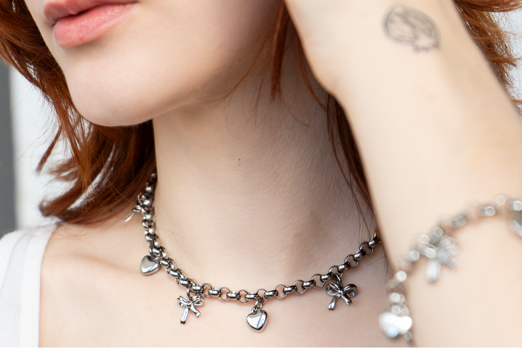 Close-up of a person wearing a delicate silver necklace with heart and flower charms.