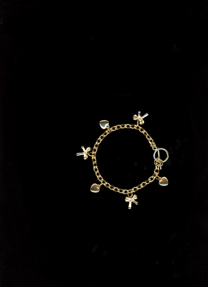 Gold bracelet with 3-d bow and heart charms on a black background