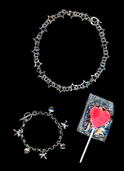 Chainmail star necklace and charm bracelet with 3-d bow and heart charms on a black background with a bright pink heart shaped lollypop