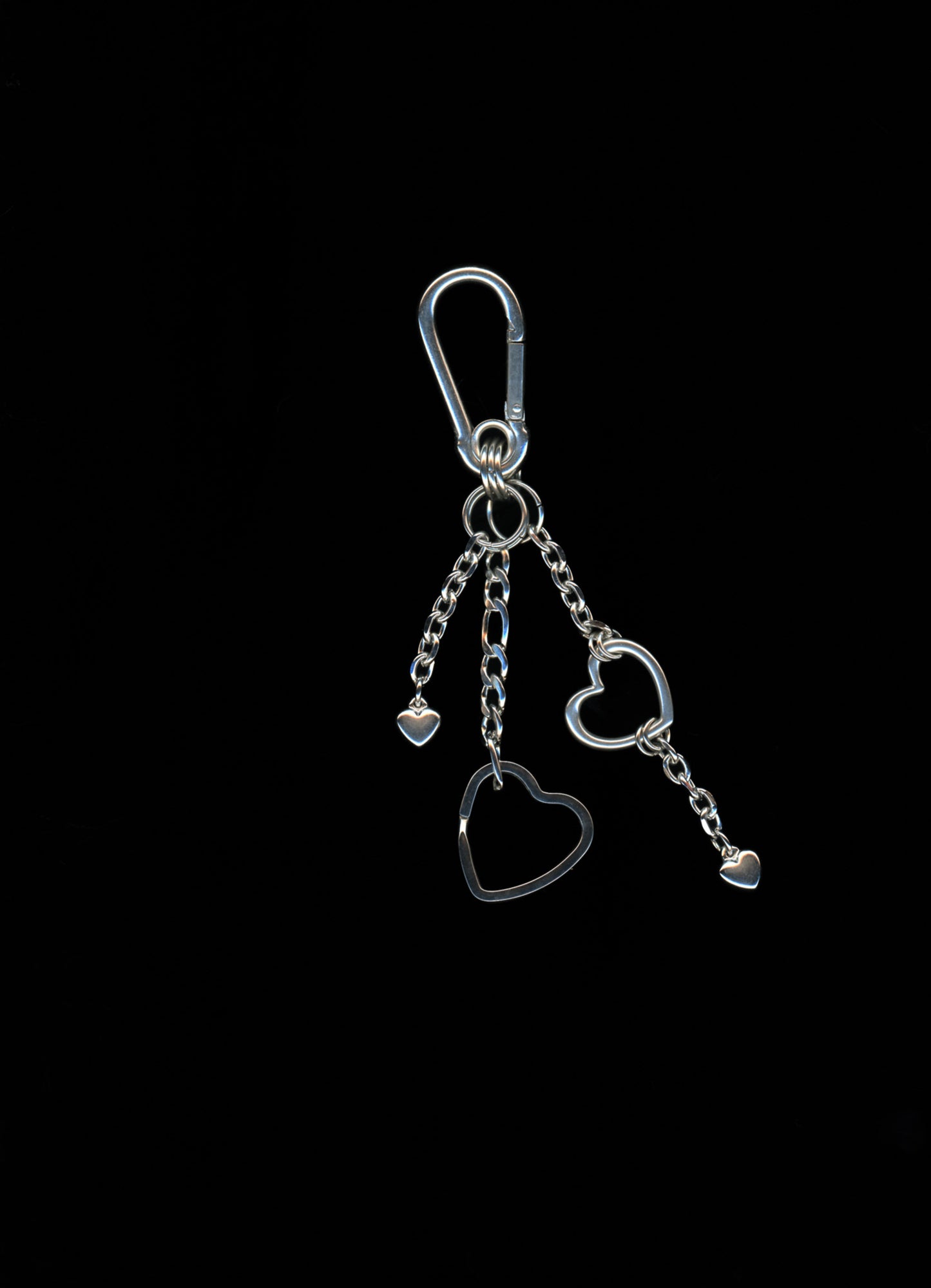 A silver stainless steel heart-shaped carabiner keychain with additional heart charms and Figaro chains on a dark background.