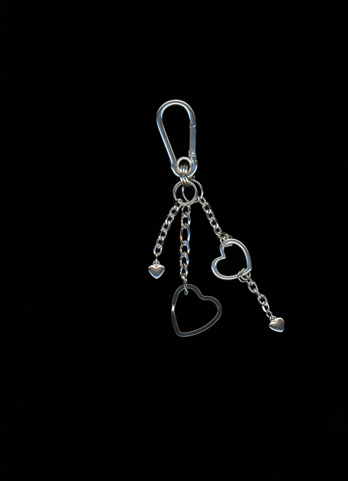 A silver stainless steel heart-shaped carabiner keychain with additional heart charms and Figaro chains on a dark background.