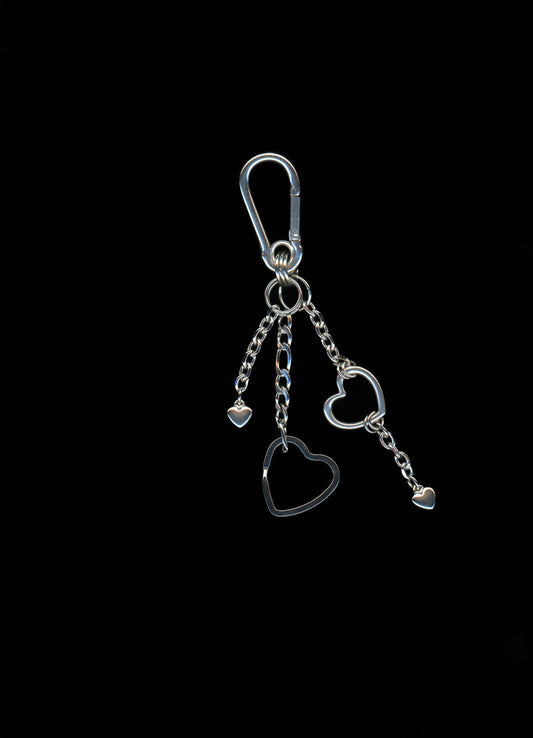 A silver stainless steel heart-shaped carabiner keychain with additional heart charms and Figaro chains on a dark background.
