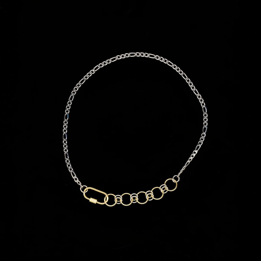 Gold and silver figaro chain neckalce with gold carabiner chainmail and carabiner closure detail on a black background