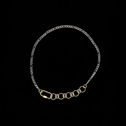 Gold and silver figaro chain neckalce with gold carabiner chainmail and carabiner closure detail on a black background