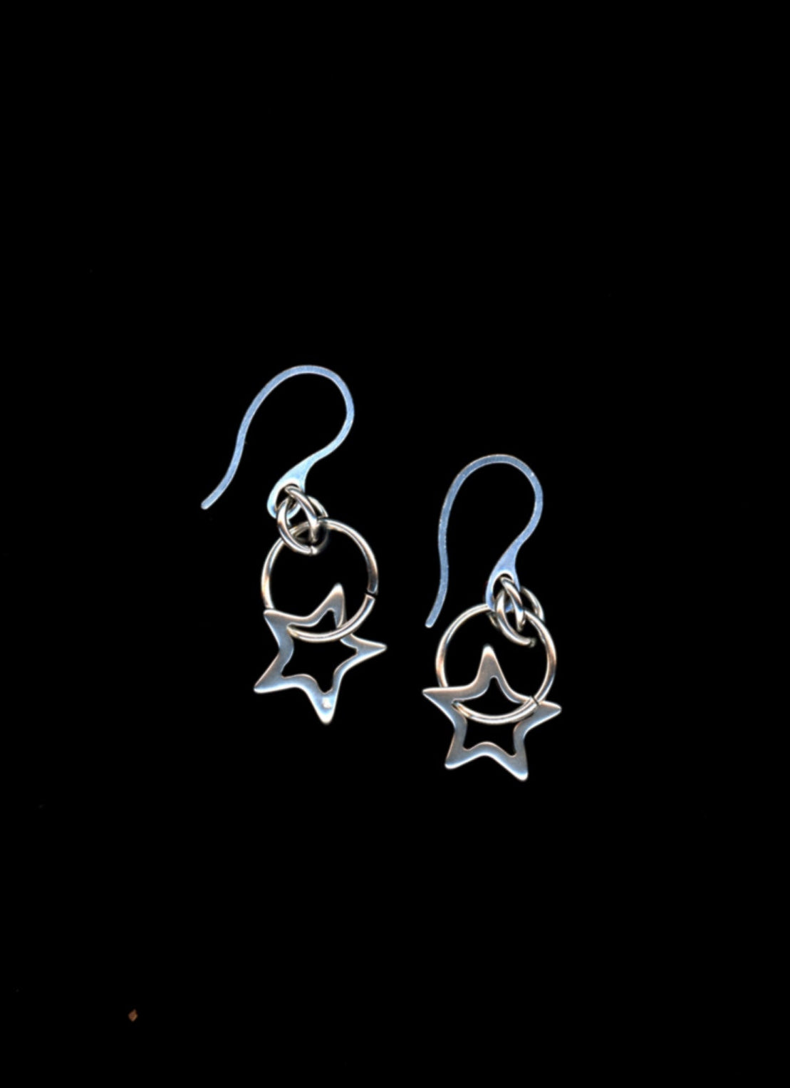 Pair of silver earrings with star outline charms on a black background