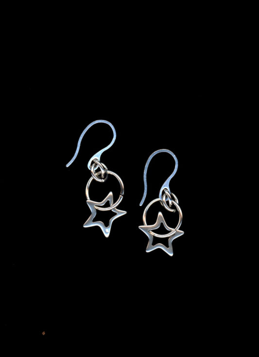 Pair of silver earrings with star outline charms on a black background