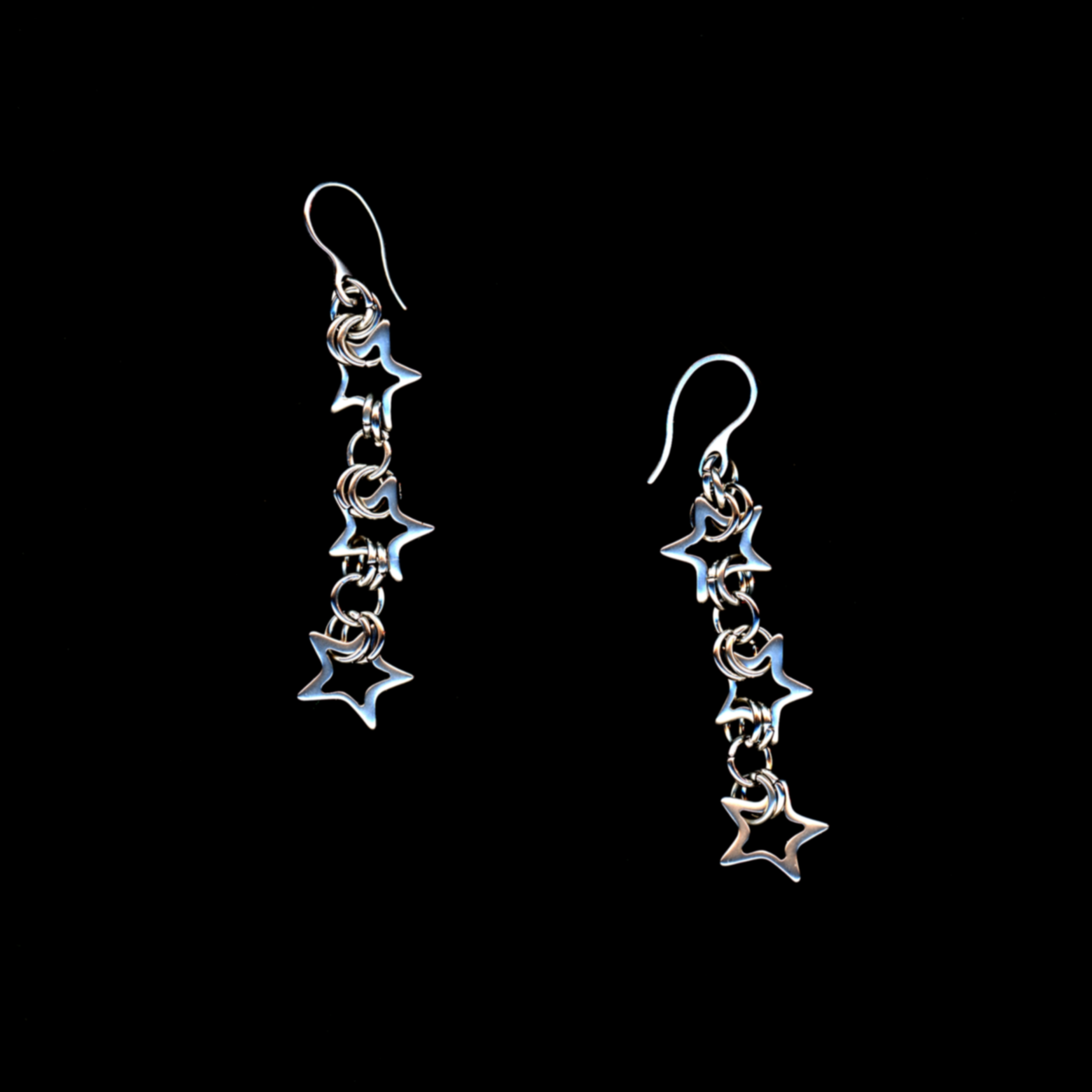 This image features a pair of elegant petite starlight viper earrings. Each earring is composed of a series of star-shaped links, connected to form a chainmail design, which cascades elegantly from the classic ear wire.