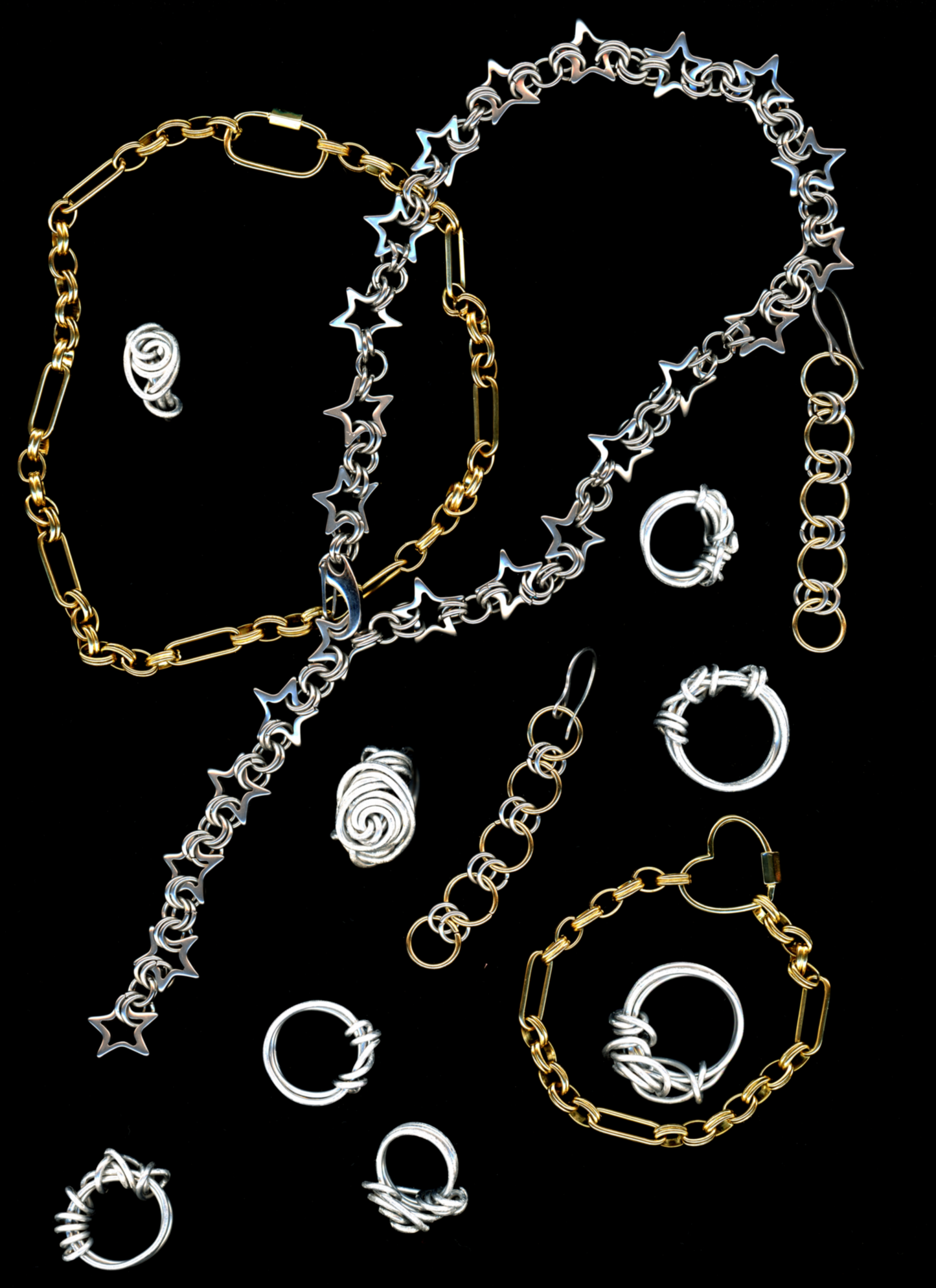 A stainless steel star chainmail necklace with a spring closure clasp, and other bywolfgang chain necklaces, earrings, and bracelets displayed against a black background.