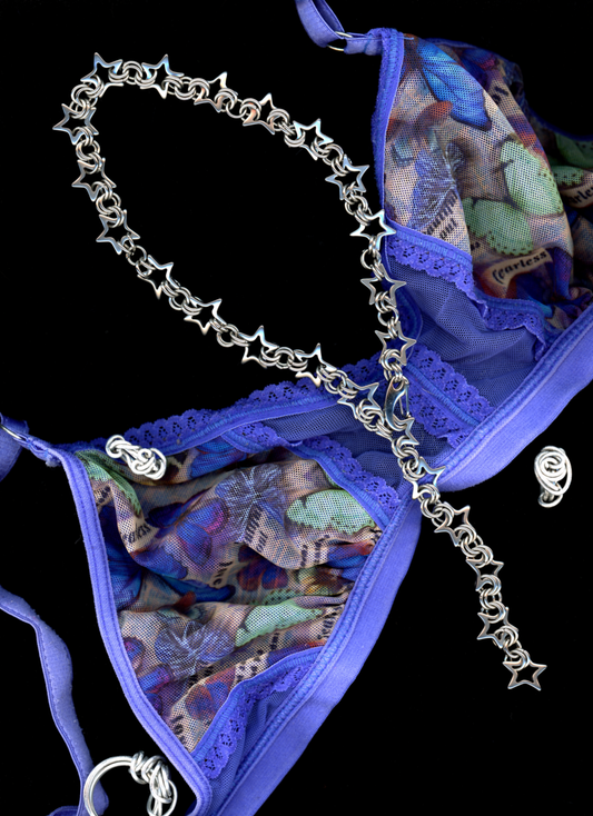 A stainless steel star chainmail necklace with a spring closure clasp, with a blue butterfly print bralette and a few continuous thread rings displayed against a black background.