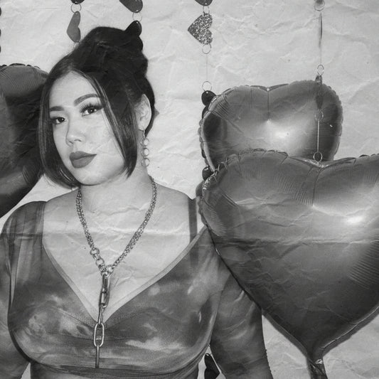 racheal wears the trinity drop earrings and aria necklace in a v neck top and high bun with bangs surrounded by heart shaped balloons and garlands in a black and white edit 